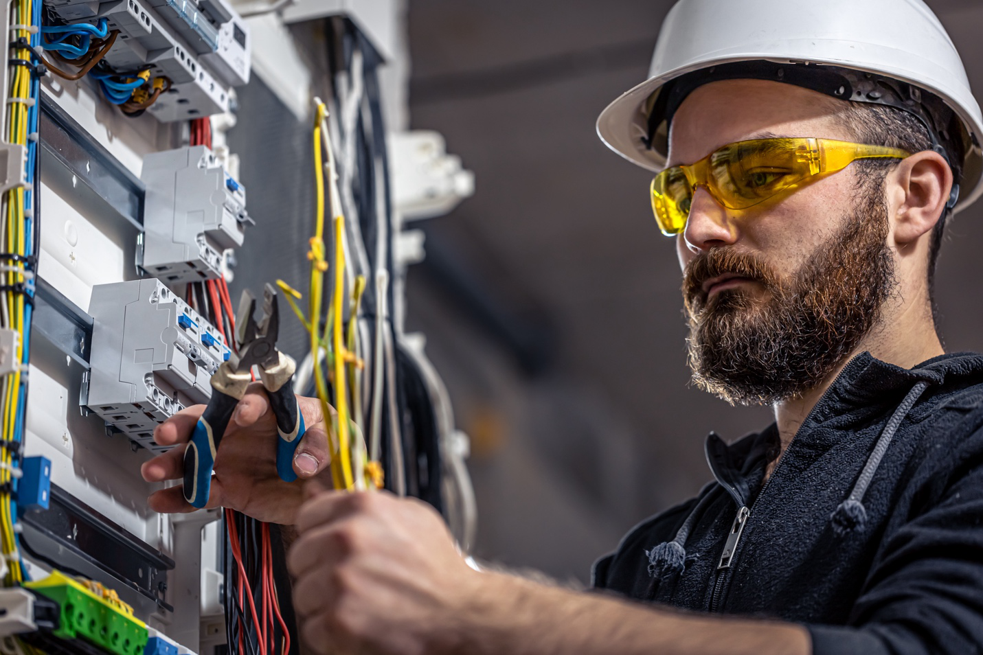 An electrician wearing safety goggles and hard hat holds wire to crimp it.