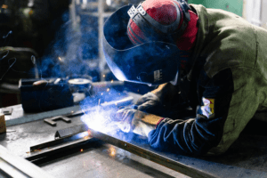 Temporary skilled laborer welding metal bars at a worksite while wearing PPE