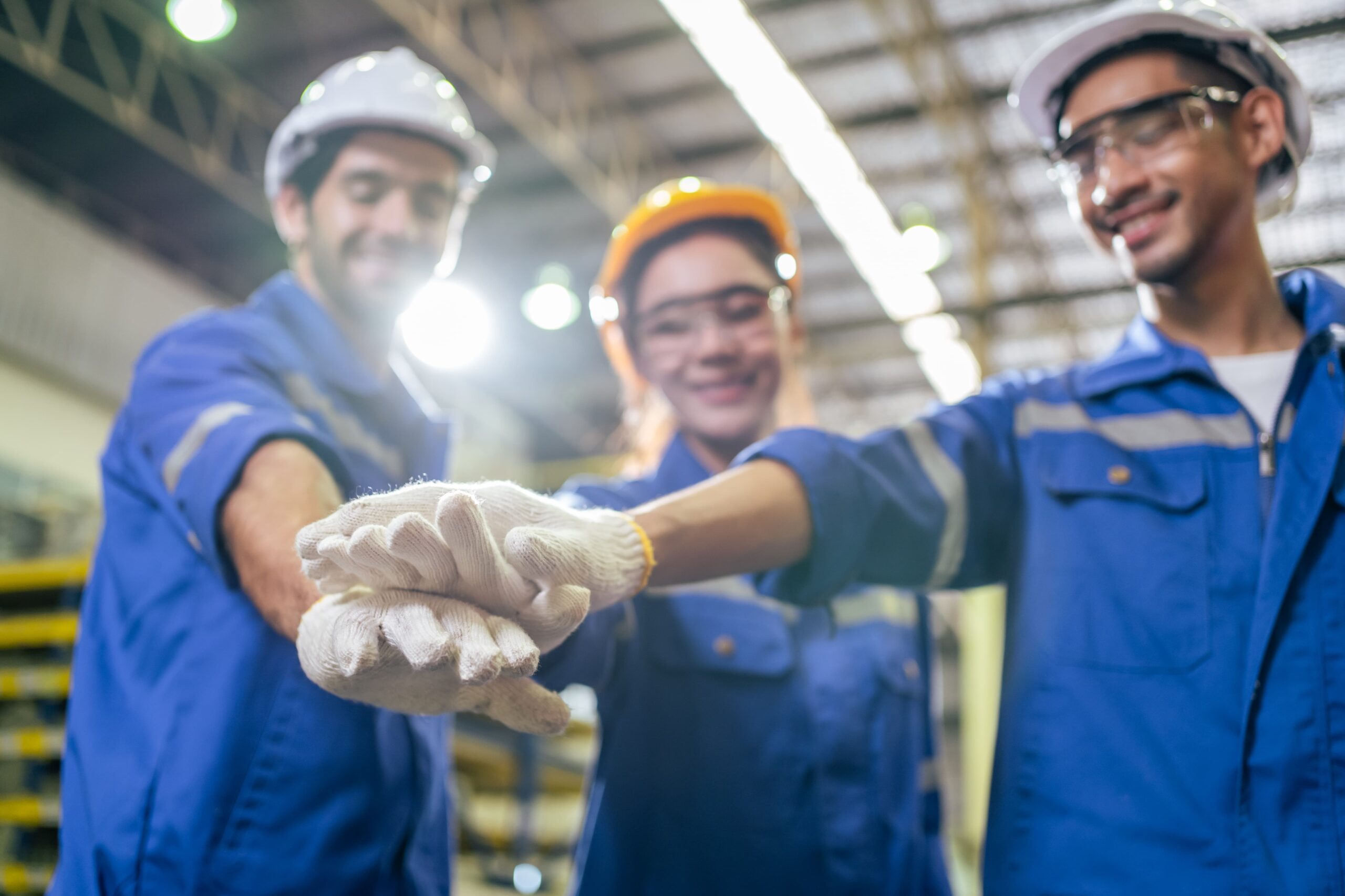 three general labor workers in blue overalls stand with their hands stacked