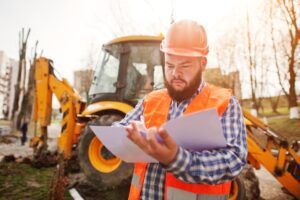 a construction worker looks at a plan sheet standing in front of a tractor