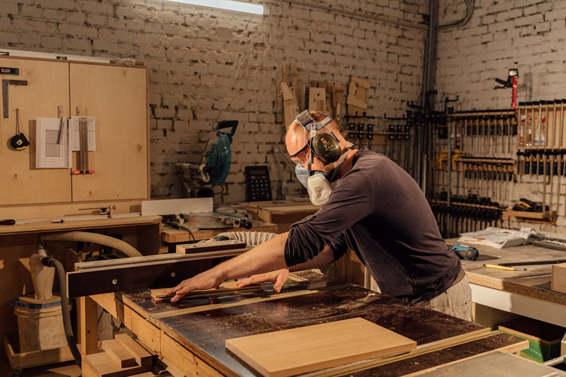 A person wearing PPE and measuring wood in a workshop.