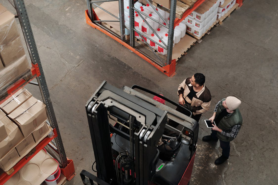 Two industrial laborers standing with machinery in a warehouse