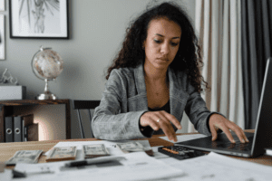 A woman using laptop and calculator with cash stacks by her side