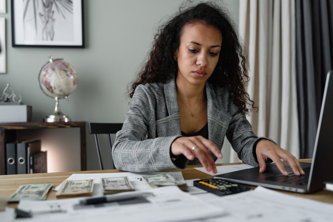 A woman using laptop and calculator with cash stacks by her side