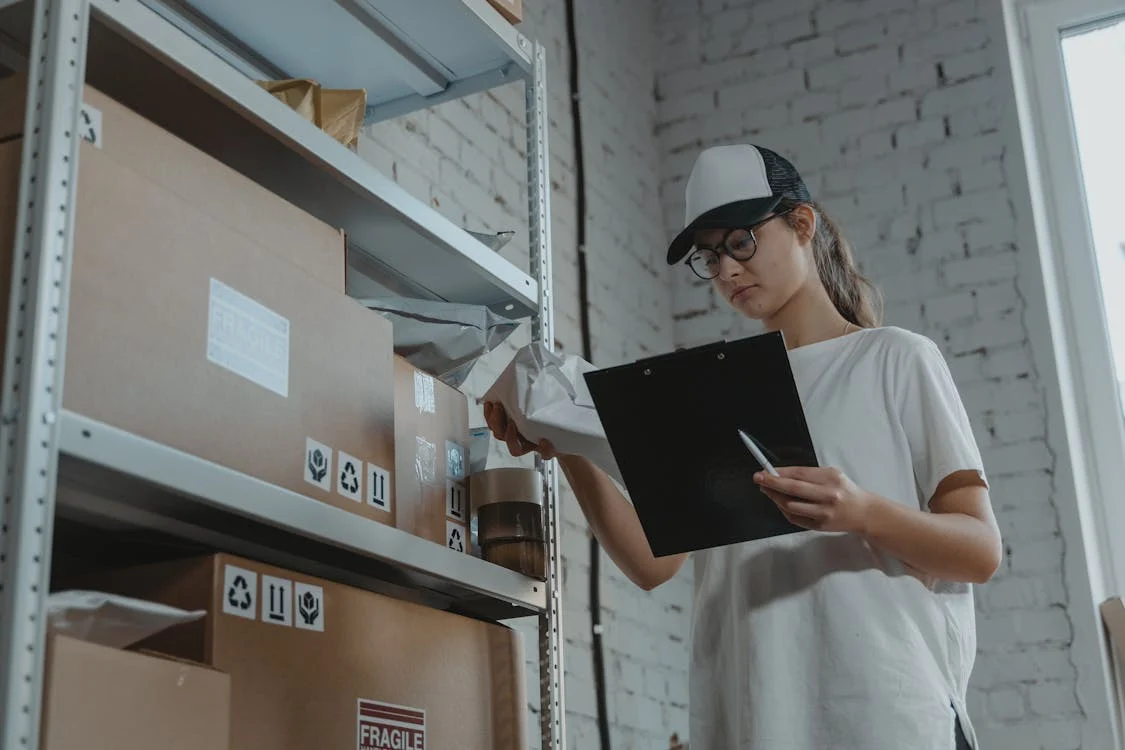 A person holding a tablet and a crumpled-up paper, standing next to cartons.