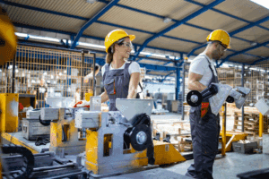 People using machines in a factory setting while wearing personal protective equipment (PPE)