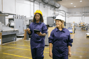 Two people in protective helmets, with one holding a tablet