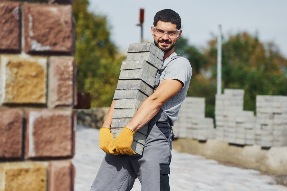 A general laborer on a worksite carrying a stack of pavers